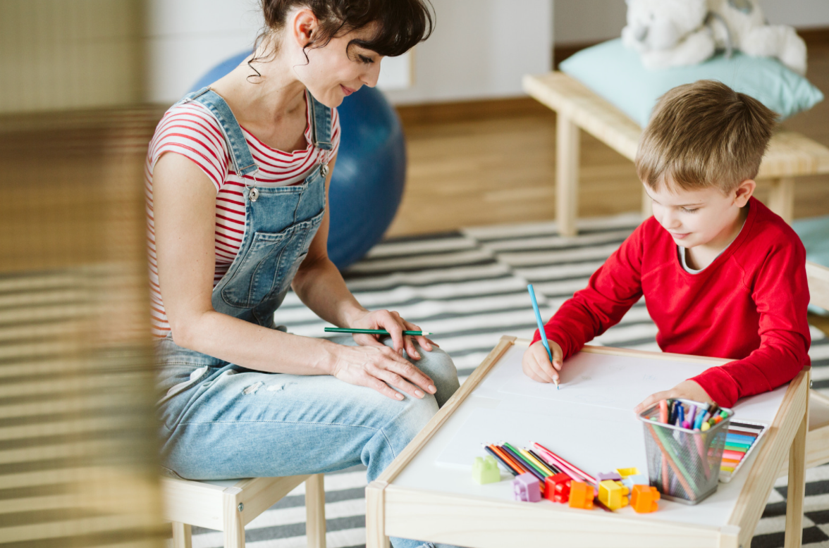 child coloring on paper with parent sitting in chair