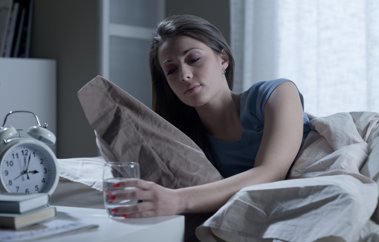 woman awake holding glass near alarm clock